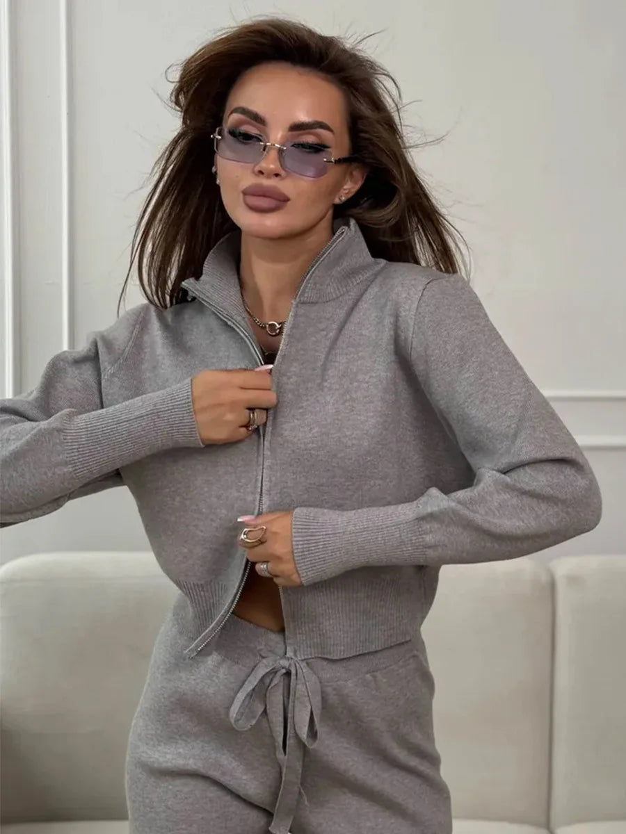 Mujer con el conjunto gris y zapatillas blancas, con la chaqueta corta cerrada sobre la cinturilla del pantalón