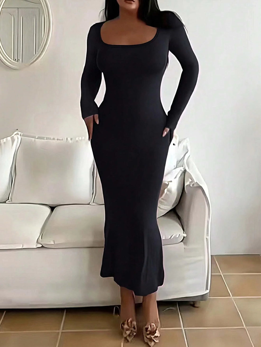 Modelo con el vestido largo de canalé negro, de cuerpo entero, en una sala con un sofá crema