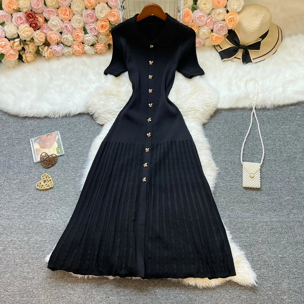 Vestido midi de canalé negro en plano, con el cuello polo, la tapeta de botones dorados y la falda de tablas