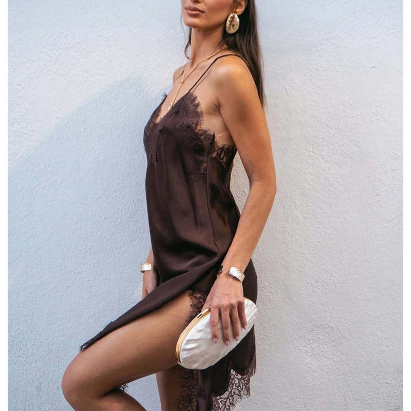 Modelo con el vestido lencero de satén chocolate contra una pared blanca, con un clutch blanco y la pierna asomando por la abertura