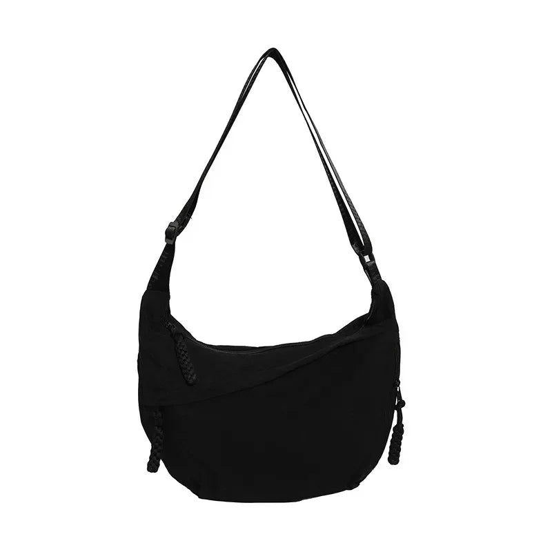 Bolso bandolera de nailon negro en forma de media luna sobre fondo blanco, con la bandolera larga extendida