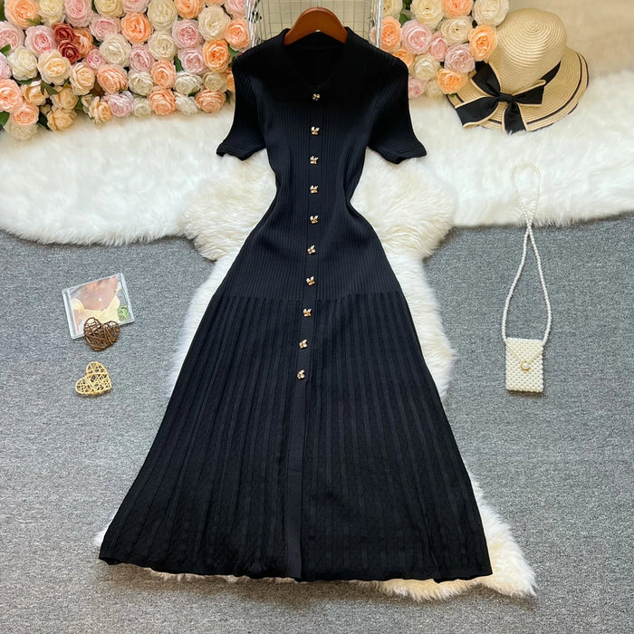 Vestido midi de canalé negro en plano, con el cuello polo, la tapeta de botones dorados y la falda de tablas